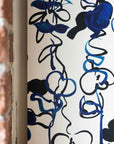 Close up Abstract floral wallpaper with hand-drawn botanical elements in deep blue and black tones on a white background, creating a dynamic and artistic design with brick wall in foreground