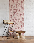 Romantic silk wallpaper with hand-drawn red bows on a soft pink background, styled with a beige barstool, rustic wooden table, and neutral decor.