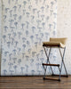 Elegant wallpaper featuring hand-drawn blue bows on a crisp white background, complemented by a beige cushioned stool with black metal legs.