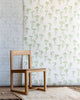 Playful wallpaper with hand-drawn green bows on a white background, styled with a natural wood chair and a textured cream rug.