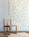 Playful wallpaper with hand-drawn green bows on a white background, styled with a natural wood chair and a textured cream rug.