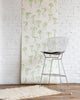 Playful silk wallpaper with hand-drawn green bows on a white background, styled with a modern wireframe barstool and a textured cream rug.