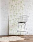 Playful silk wallpaper with hand-drawn green bows on a white background, styled with a modern wireframe barstool and a textured cream rug.