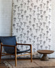 Minimalist wallpaper featuring black hand-drawn bows on a white background, styled with a black leather and wood lounge chair in a rustic interior.