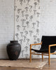 Minimalist silk wallpaper featuring black handdrawn bows on a white background, styled with a black leather and wood chair and a large rustic vase.