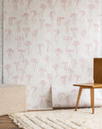 Feminine wallpaper with delicate pink hand-drawn bows on a white background, styled with a boucle ottoman, wooden chair, and a plush cream rug.