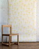 Cheerful wallpaper with hand-drawn yellow bows on a white background, styled with a natural wood chair and rustic wood flooring.