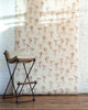 Neutral-toned wallpaper with hand-drawn brown bows on a warm beige background, complemented by a beige leather barstool with wooden accents in a rustic interior setting.