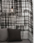 Cozy nook with black and white hand-painted plaid wallpaper, complemented by a minimalist pendant light, dark gray cushions, and soft drapery.
