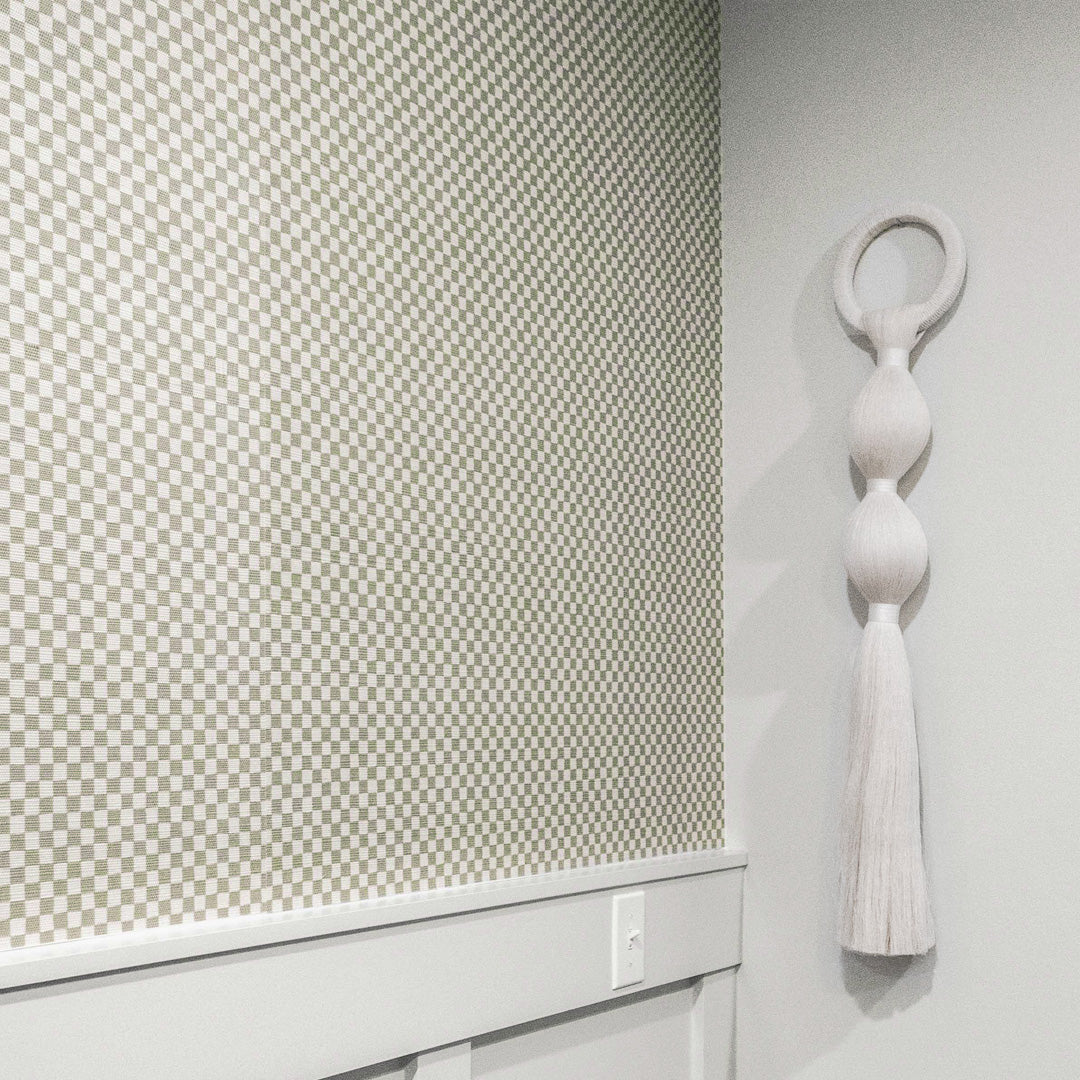 Sage green and white checkered wallpaper with a woven texture, styled with white wainscoting and a sculptural wall hanging for a modern, organic aesthetic.