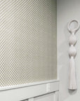 Sage green and white checkered wallpaper with a woven texture, styled with white wainscoting and a sculptural wall hanging for a modern, organic aesthetic.