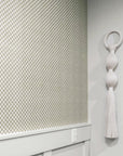 Sage green and white checkered wallpaper with a woven texture, styled with white wainscoting and a sculptural wall hanging for a modern, organic aesthetic.
