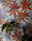 wallpaper with large abstract neutral floral pattern in warm orange, red, and blue tones; green houseplant leaves in a ceramic planter in the foreground.