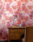 Full view of a home office with red floral wallpaper, vintage wooden desk, glass-domed brass table lamp, yellow notebook, and a tan leather chair.