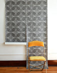 Gray geometric wallpaper with curved circular overlapping shapes, featuring delicate dotted texturing and abstract interconnected design, with yellow folding chair in foreground