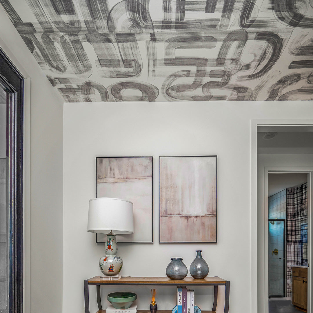 Modern entryway featuring an abstract brushstroke Down the Rabbit Hole wallpaper applied to the ceiling, with a neutral-toned console table, decorative vases, and framed artwork on the wall.
