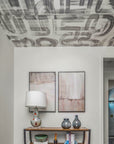 Modern entryway featuring an abstract brushstroke Down the Rabbit Hole wallpaper applied to the ceiling, with a neutral-toned console table, decorative vases, and framed artwork on the wall.