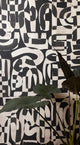 Close-up of black and white grasscloth wallpaper with bold, abstract brushstroke patterns, partially obscured by large green tropical leaves.