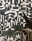 Close-up of black and white grasscloth wallpaper with bold, abstract brushstroke patterns, partially obscured by large green tropical leaves.