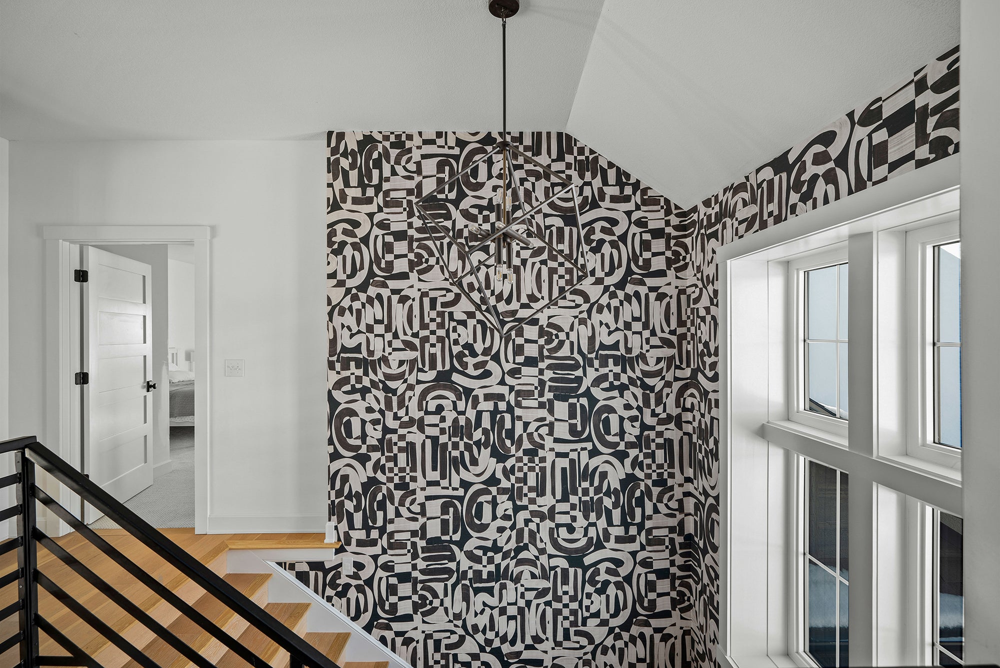 Stairwell with grasscloth wallpaper featuring an abstract black and white geometric pattern, contrasted against white walls and large windows.