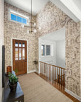 Entryway with neutral-toned grasscloth wallpaper featuring an abstract geometric design, high ceilings, a modern chandelier, and wood accents.