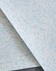 Overlapping wallpaper samples with a soft blue and white intricate feather-like design, showcasing the texture and pattern.