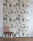 Grasscloth wallpaper of a large floral printed on grasscloth, staged on a white brick wall with a wooden chair