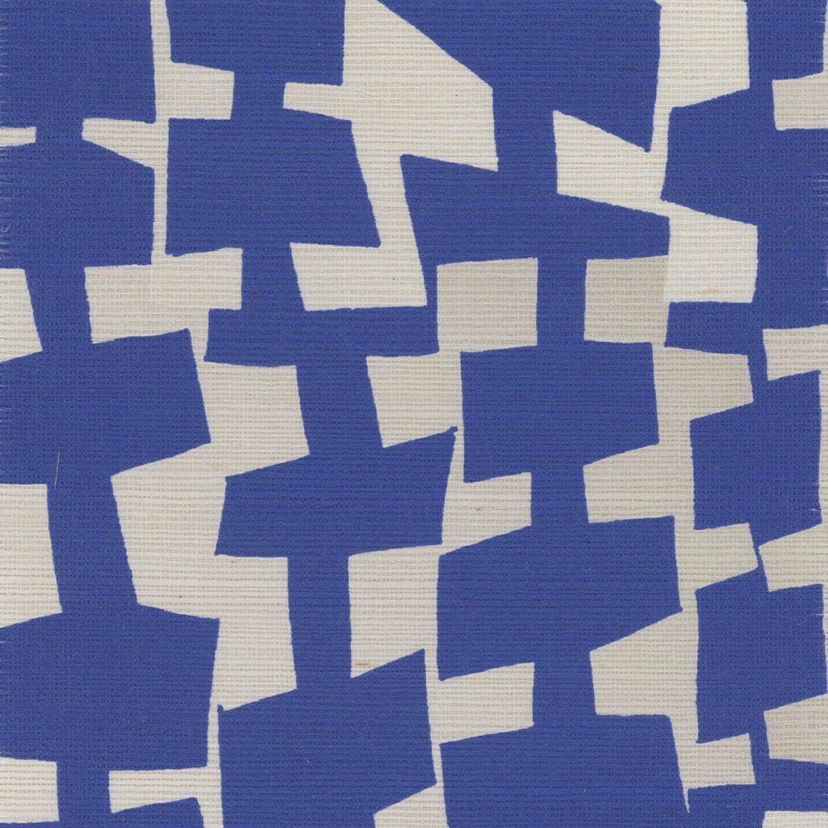 A close-up of geometric-patterned grasscloth wallpaper in deep blue and off-white, with abstract, irregularly shaped blocks forming a bold, contemporary design.