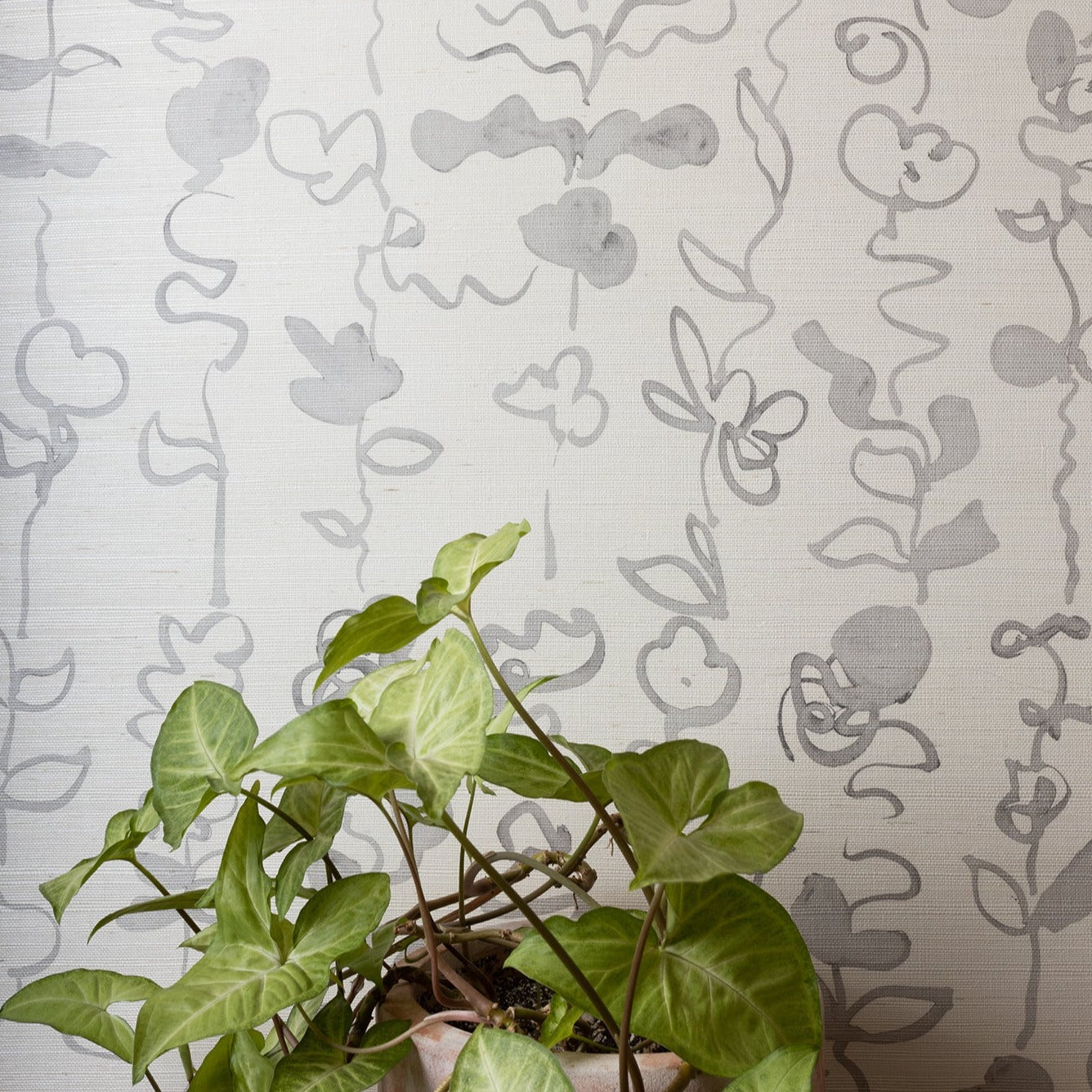 Interior setting with grasscloth wallpaper in soft gray botanical floral stripe, paired with a potted green plant for a natural aesthetic.