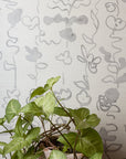 Interior setting with grasscloth wallpaper in soft gray botanical floral stripe, paired with a potted green plant for a natural aesthetic.