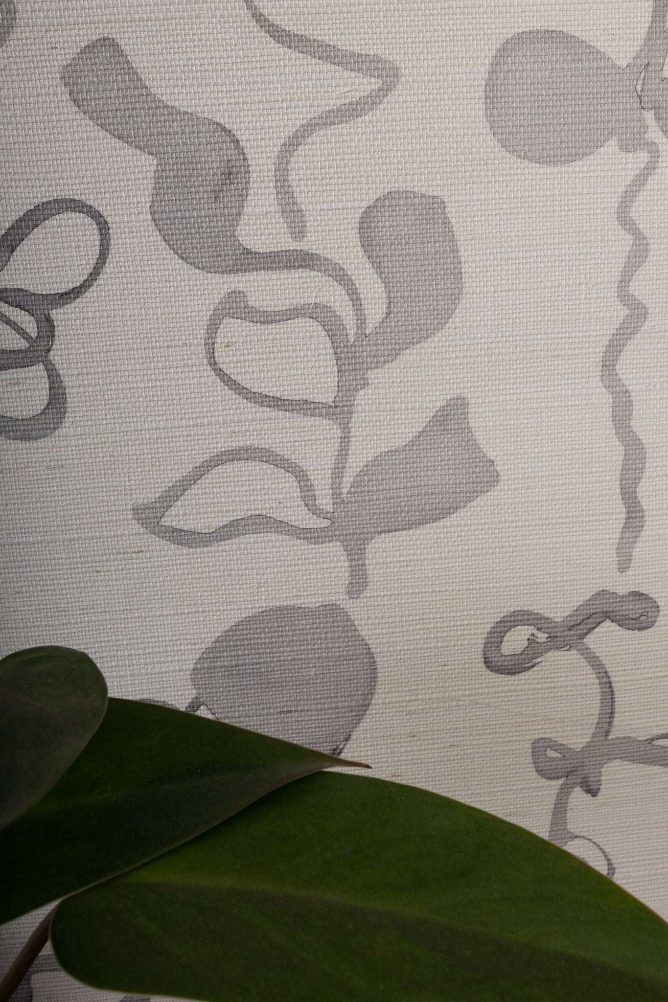 Extreme close-up of grasscloth wallpaper with an abstract gray floral pattern, highlighting its intricate woven texture. Green leaf in foreground