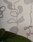 Extreme close-up of grasscloth wallpaper with an abstract gray floral pattern, highlighting its intricate woven texture. Green leaf in foreground