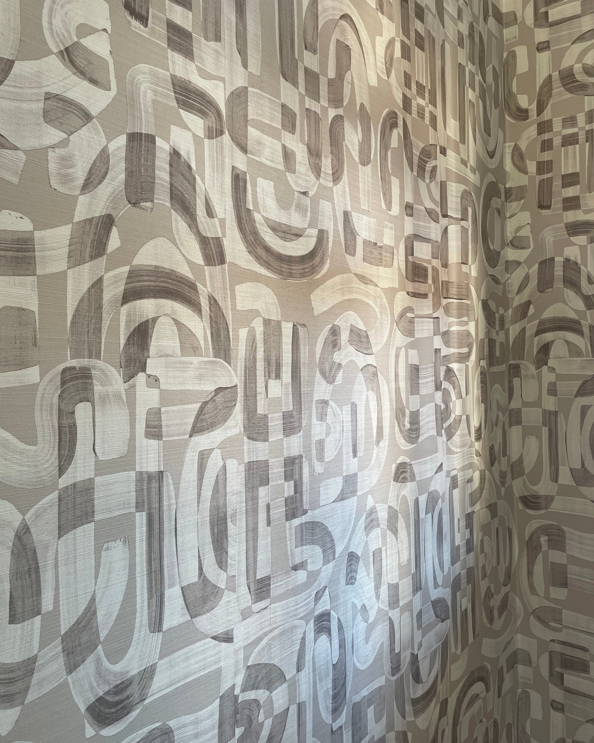 Close-up of taupe-colored grasscloth wallpaper with an abstract, hand-painted geometric pattern, featuring overlapping brushstrokes and organic shapes.