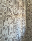 Close-up of taupe-colored grasscloth wallpaper with an abstract, hand-painted geometric pattern, featuring overlapping brushstrokes and organic shapes.