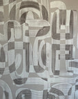 Close-up of taupe and white grasscloth wallpaper featuring an abstract brushstroke pattern with overlapping curved and geometric shapes.