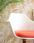 Golden yellow and white tropical leaf wallpaper with a subtle ripple texture, styled with a white modern chair and a potted palm.