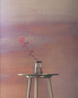 Warm-toned gradient wallpaper in soft mauve and peach hues, creating a sunset-inspired backdrop for a delicate red-leafed branch in a glass vase.