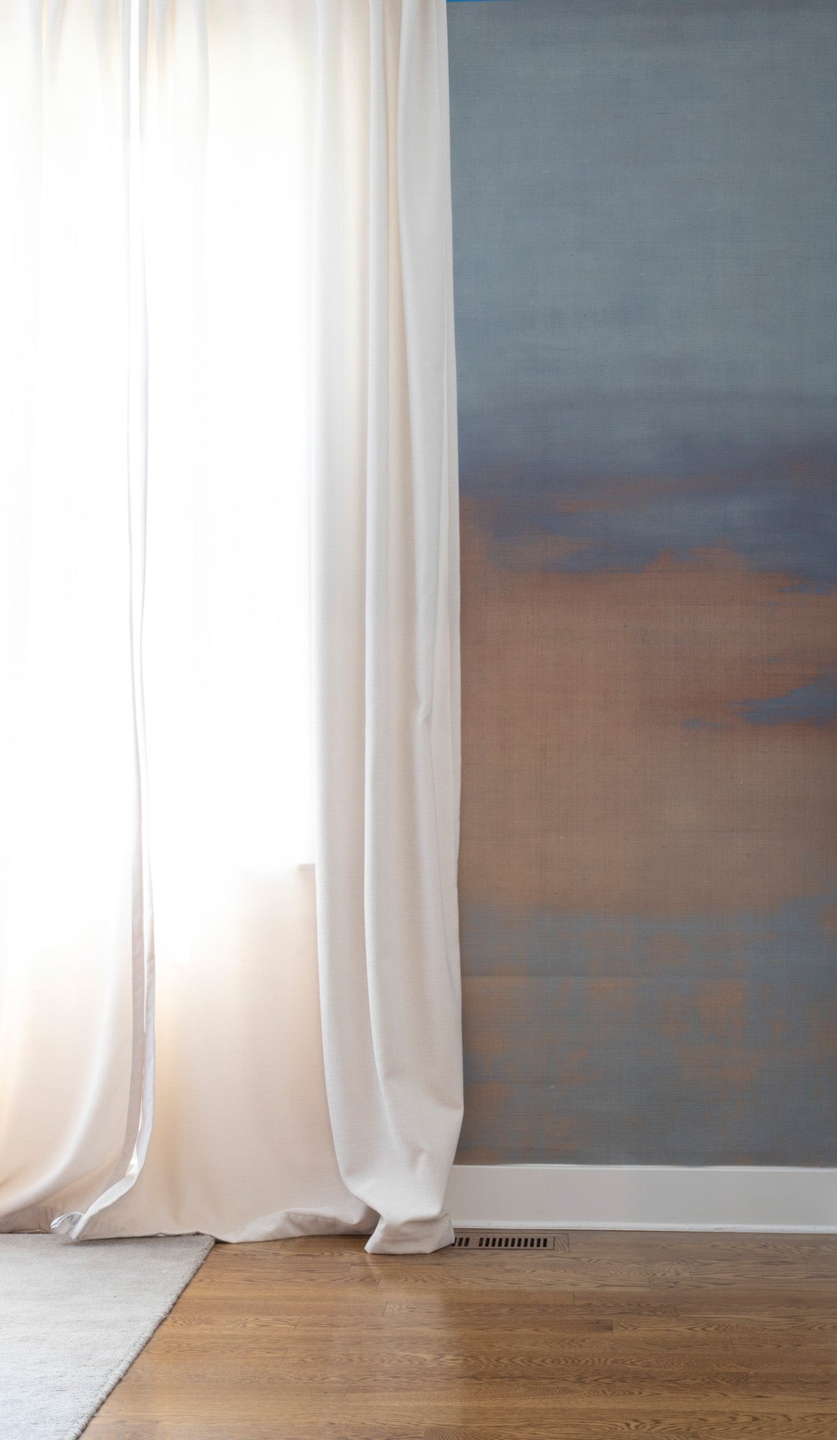 Neutral-toned ombré wallpaper with soft blue and taupe gradients, styled beside airy white curtains in a minimal interior.