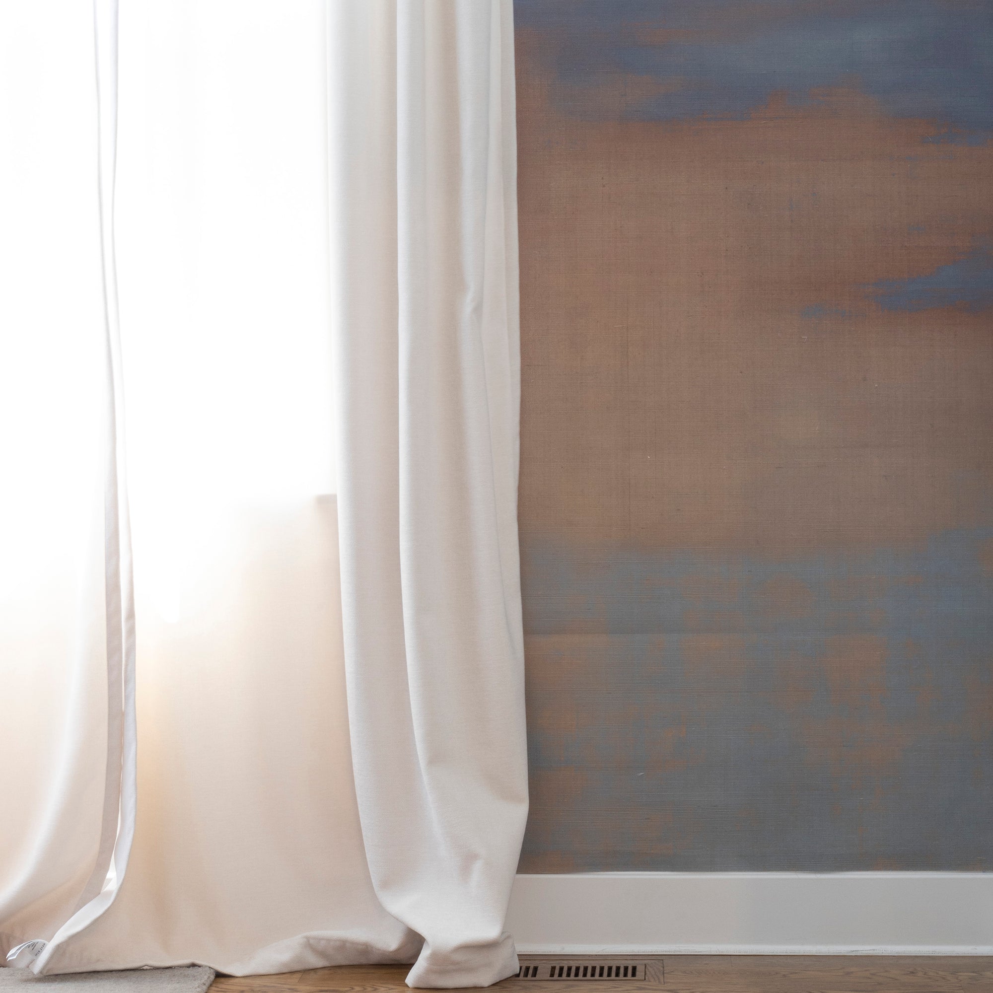 Neutral-toned ombré wallpaper with soft blue and taupe gradients, styled beside airy white curtains in a minimal interior.