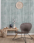 Bohemian-style living room with a green textured wallpaper featuring vertical brushstroke stripes, decorated with woven baskets, vases, and a rattan chair.