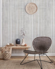 Bohemian-style living room with a soft beige textured wallpaper featuring vertical brushstroke stripes, paired with woven baskets, vases, and a rattan chair.