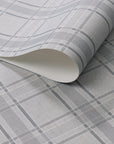 Light grey wallpaper with a classic plaid pattern in soft charcoal and white tones, shown in a rolled detail to highlight texture and print.