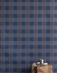 Interior scene with a wooden block side table and metal drinkware in front of a deep navy plaid wallpaper for a cozy, masculine look.
