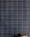 Interior scene with a wooden block table and dark accessories set against a moody charcoal plaid wallpaper for a refined, masculine look.