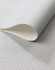 Close-up of a roll of wallpaper with soft blue and ivory vertical pinstripes on a textured linen-like surface.