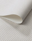 Close-up of wallpaper roll with vertical beige and off-white pinstripes, printed on a textured linen surface.