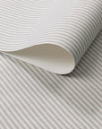 Close-up of wallpaper roll featuring narrow sage green and cream stripes on a natural linen.