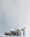 Styled interior scene with sage green and white striped linen wallpaper, paired with a marble tabletop, ceramic bowls, and neutral linens.