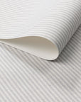 Close-up of wallpaper roll showcasing fine grey and off-white stripes on woven linen.