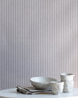 Interior scene with charcoal-striped linen wallpaper behind a marble table styled with handmade ceramic cups and a neutral linen napkin.